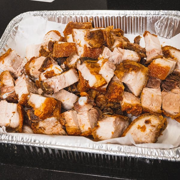 Crispy Filipino lechon kawali, deep-fried pork belly, in a foil takeout container lined with parchment paper.