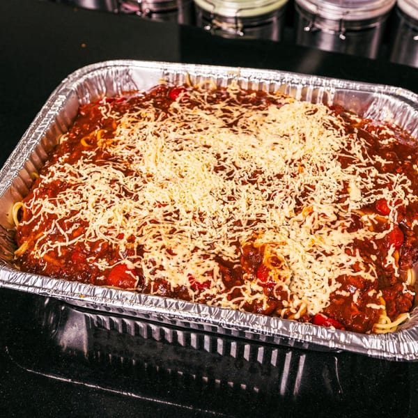 A large foil pan of Filipino spaghetti, topped with a rich red sauce and shredded cheese.