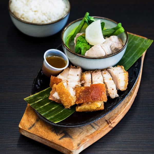 Filipino lechon kawali with crispy skin, a side of sinigang soup, and rice on a wooden board.