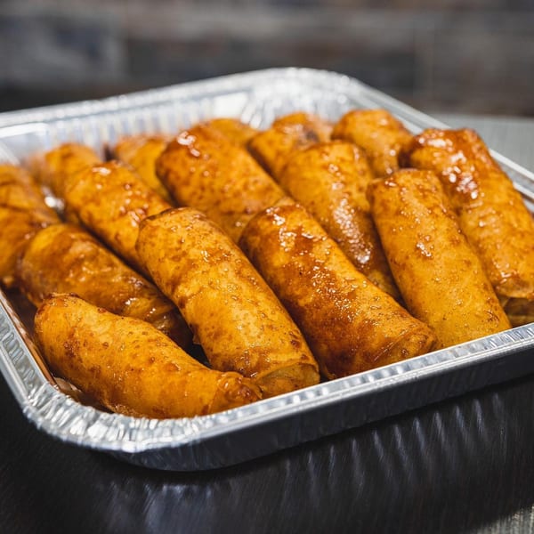 A foil tray filled with golden-brown Filipino lumpia, glistening with a sweet glaze.