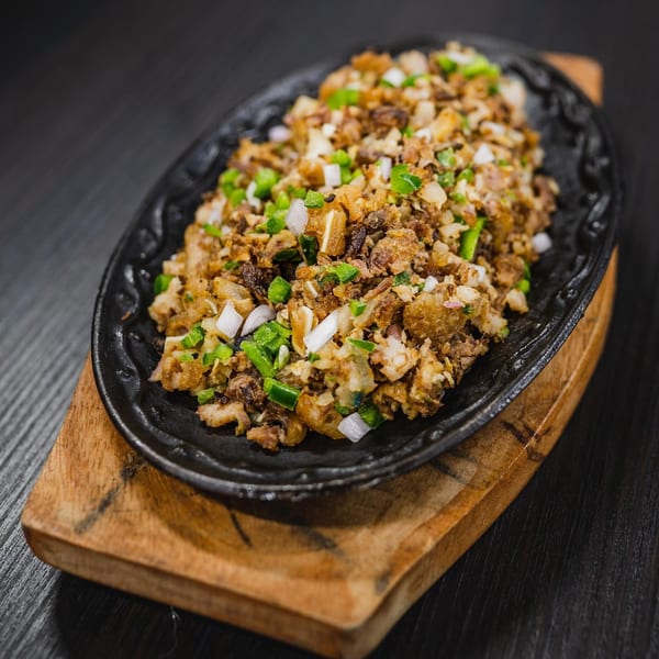 Filipino sisig, a sizzling dish of chopped meat and onions, served on a black platter.