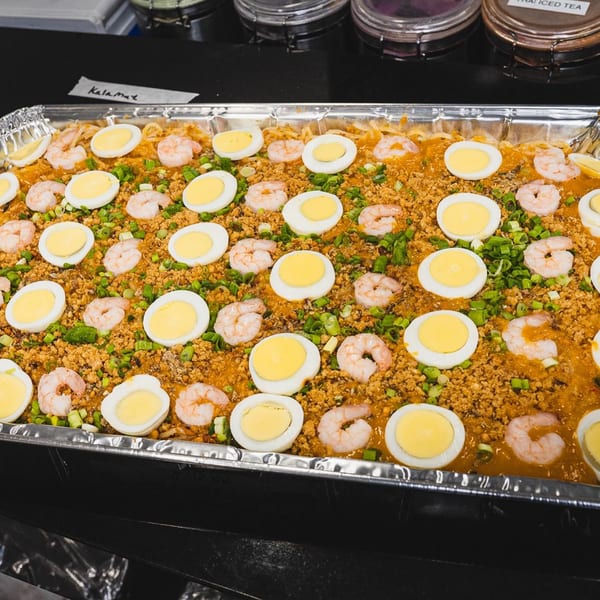 A large tray of Filipino Pancit Palabok with shrimp, eggs, and green onions.