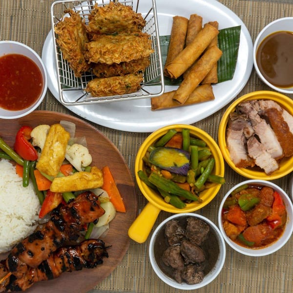 A Filipino feast with lumpia, fried tofu, grilled skewers, rice, vegetables, and various meat dishes.