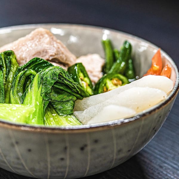 A close-up of a Filipino dish with meat, green leafy vegetables, and white daikon in a bowl.