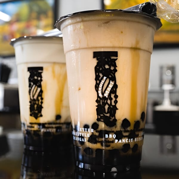 Two Manila Mart bubble tea drinks with dark tapioca pearls and creamy brown liquid.