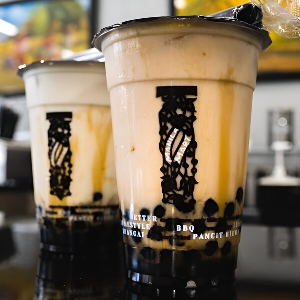 Two Manila Mart bubble tea drinks with dark tapioca pearls and creamy brown liquid.