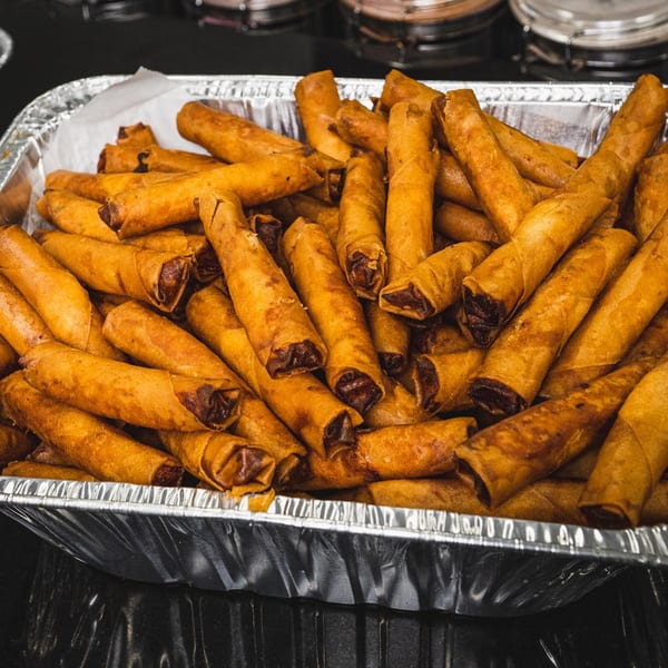 A foil tray overflowing with golden-brown Filipino lumpia, ready to be served at Manila Mart.